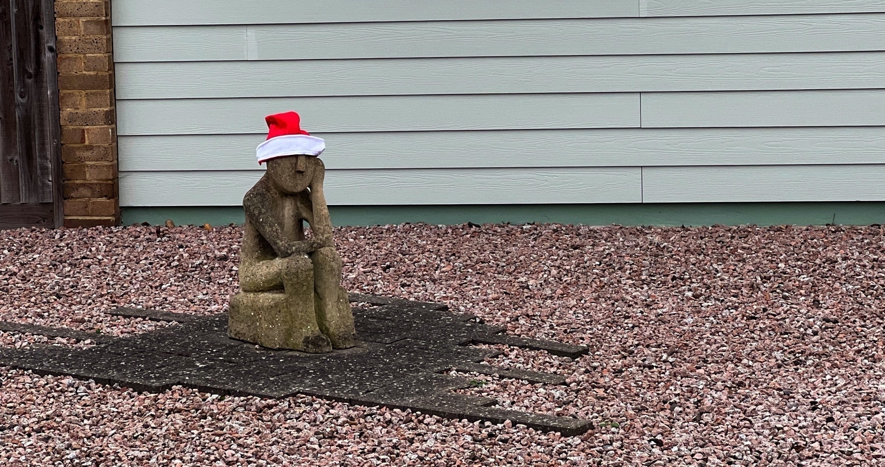 A rather miserable statue in a yard, with a santa hat on. 